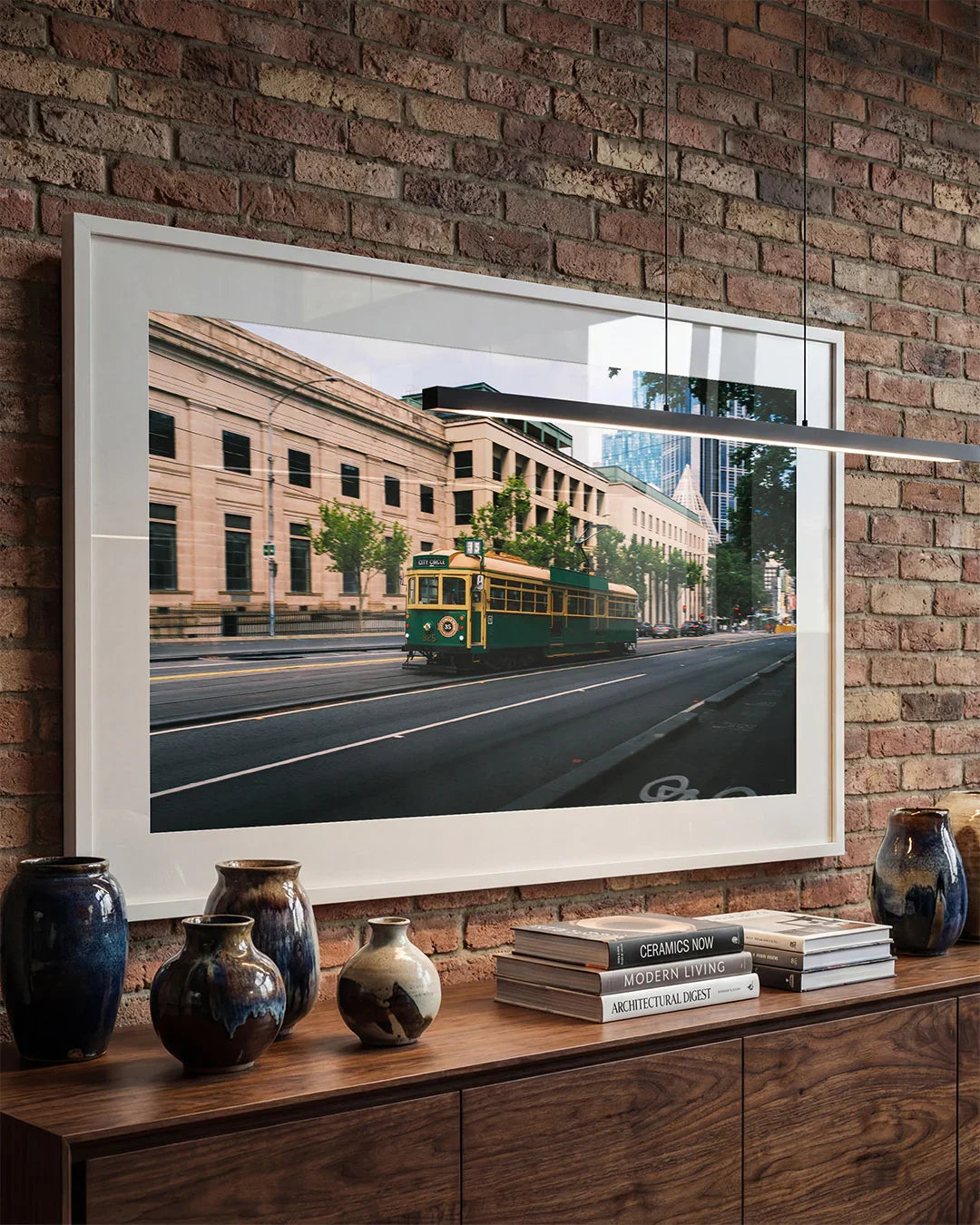 Framed Melbourne city tram print on brick wall above wooden console with ceramic vases